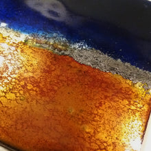 Load image into Gallery viewer, Gros plan sur le coin gauche en bas de la pièce unique en émail, ce qui fait ressortir la couleur orangé vitrifié.

