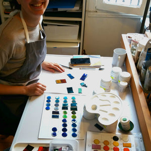 Femme souriant au bureau pendant un atelier de découverte, avec des objets de décoration en émail bleu devant elle.